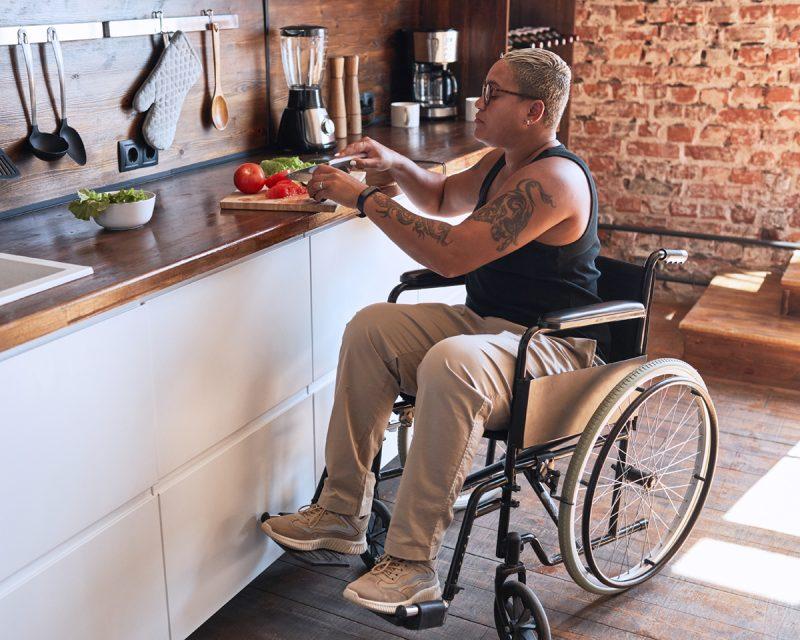 Person in a wheelchair cutting vegetables in a kitchen