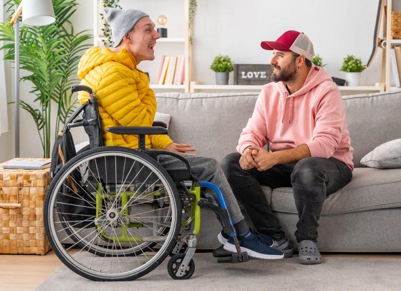 May in wheelchair laughing with a man sitting on a couch