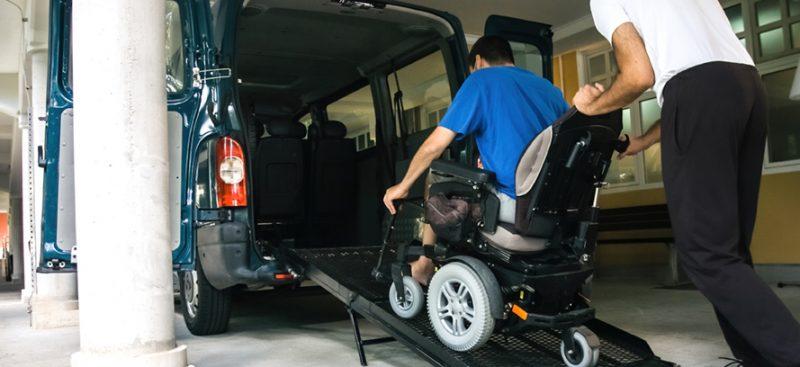 Man pushing someone in a wheelchair up a ramp into a van